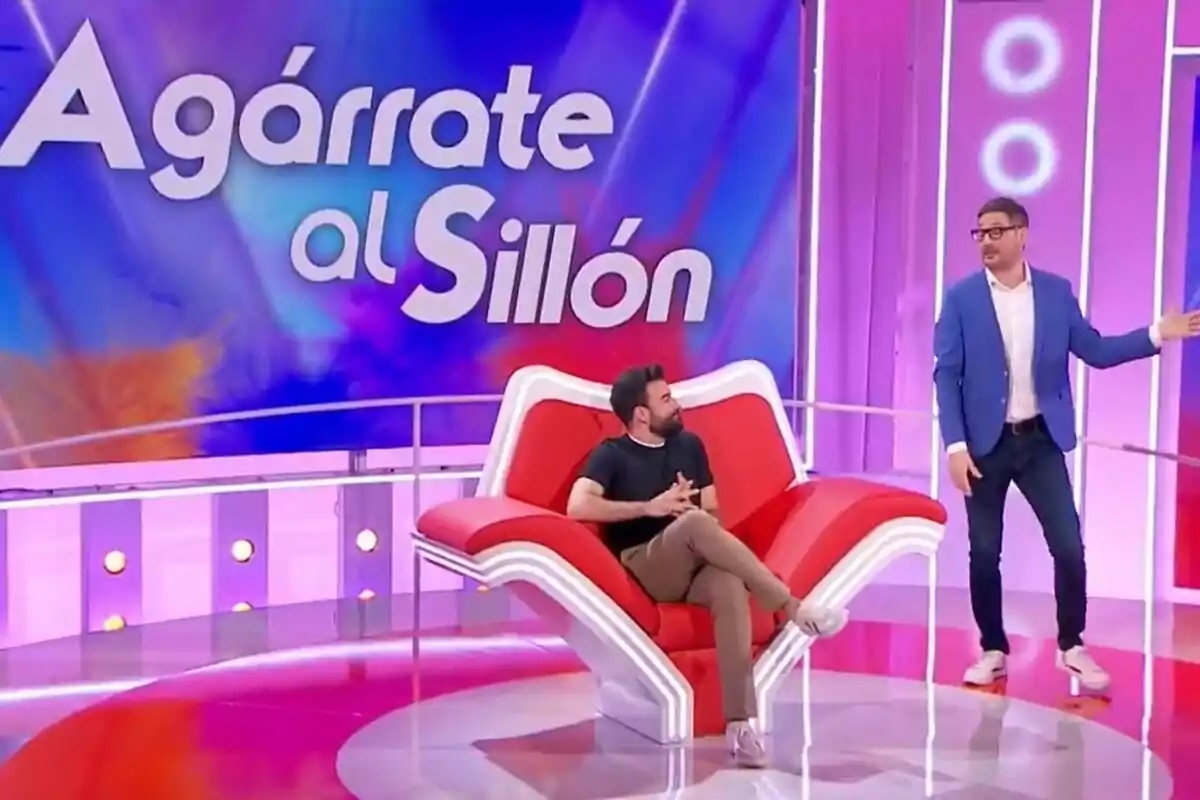 Rafa Castaño y Eugeni Alemany en un set de televisión colorido con un sillón rojo en forma de mano y un letrero grande que dice Agárrate al Sillón