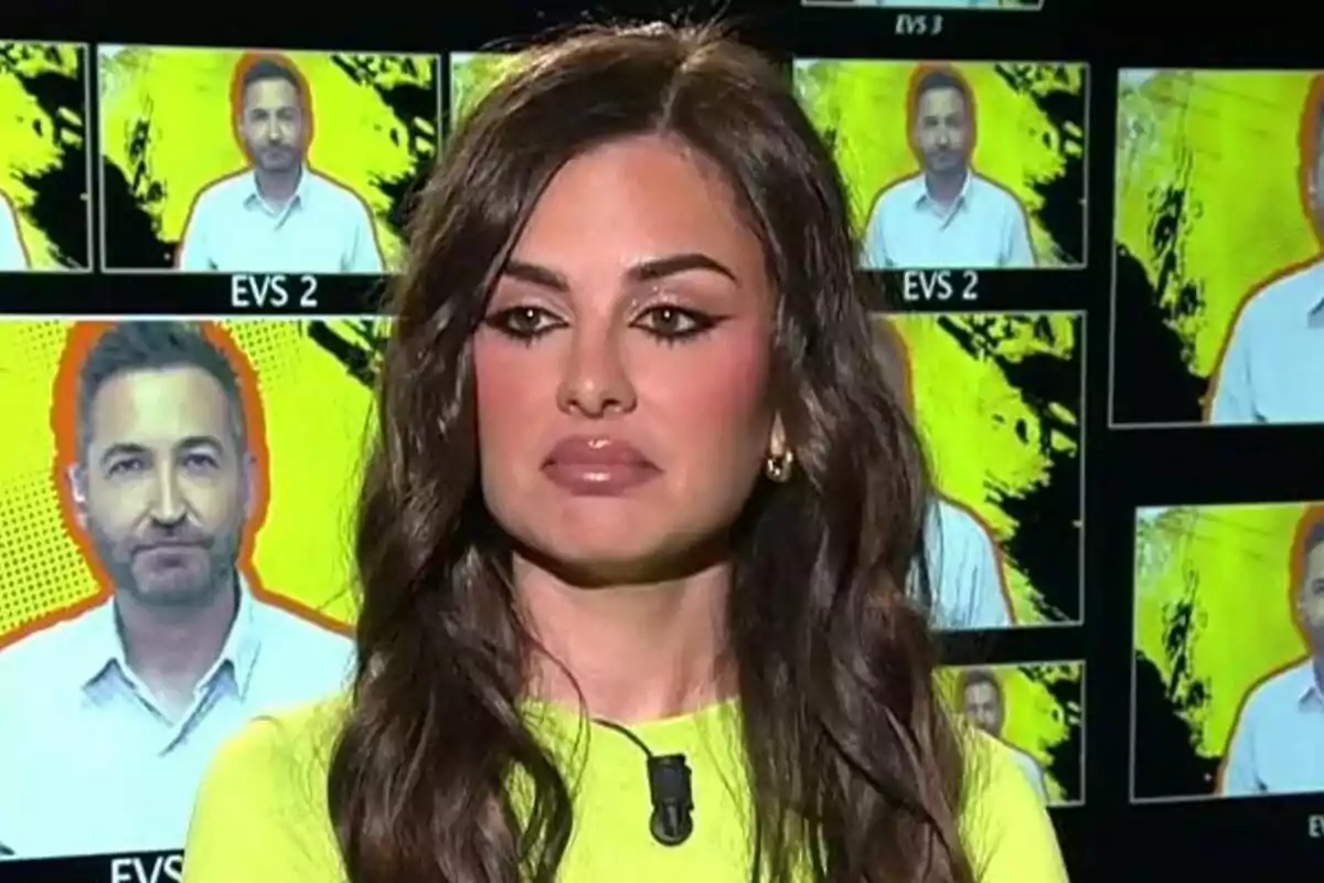 Alexia Rivas de cabello largo y oscuro con expresión seria en un estudio de Fiesta con pantallas de fondo mostrando la imagen de Frank Blanco sobre un fondo amarillo