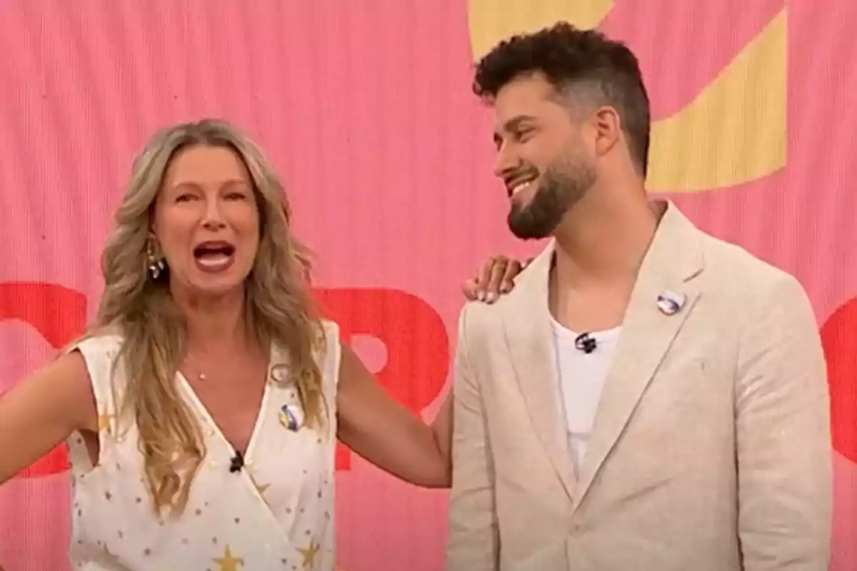 Anne Igartiburu y Javi de Hoyos sonríen y conversan en un set de D Corazón con fondo rosa