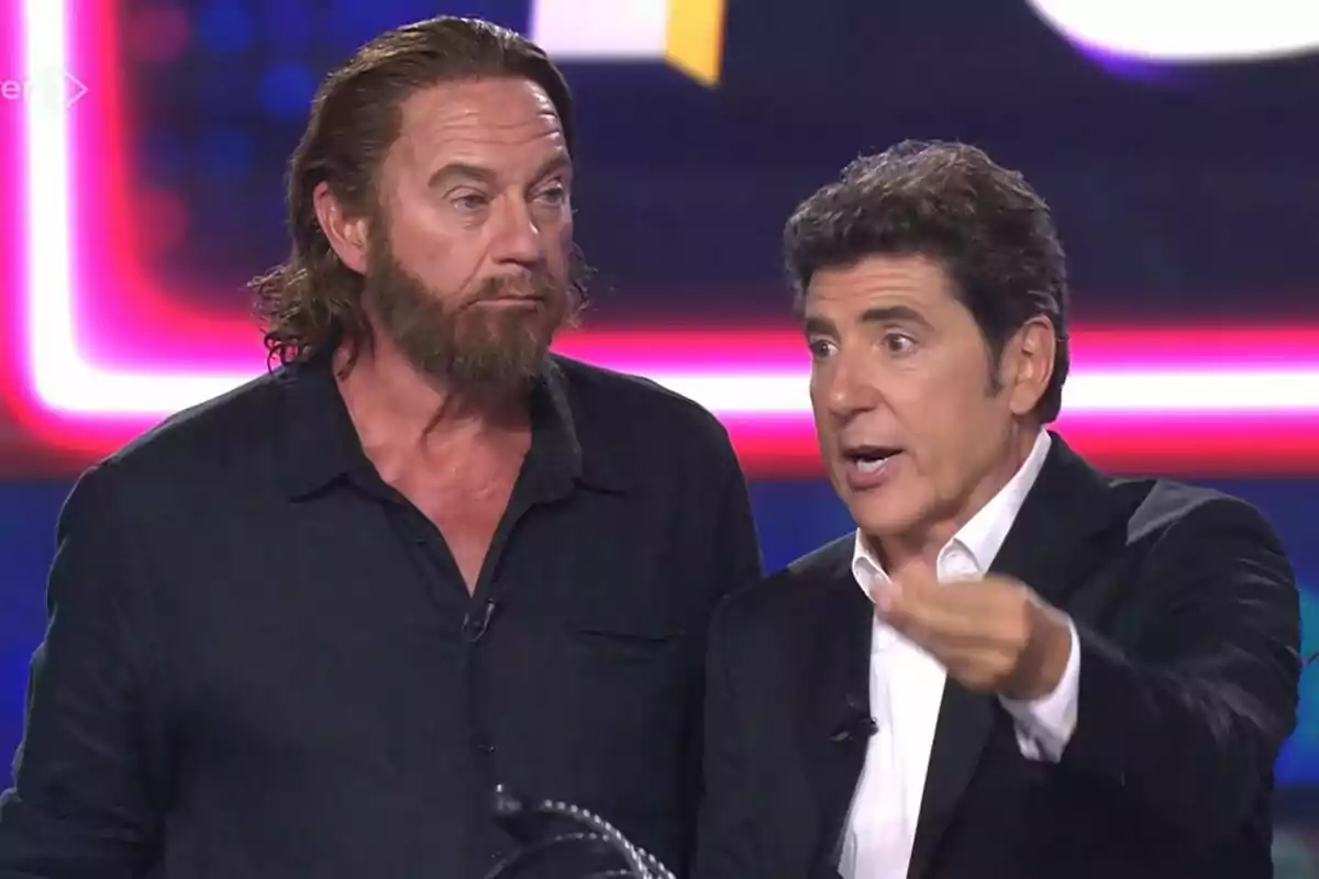 Bertín Osborne y Manel Fuentes en un set de Tu Cara Me Suena con luces de colores al fondo uno de ellos gesticulando mientras habla
