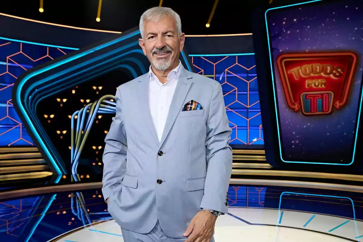 Carlos Sobera de cabell canós i barba vestit amb un vestit blau clar posant en un plató de televisió colorit amb el rètol Tots per tu al fons Carlos Sobera de cabell canós i barba vestit amb un vestit blau clar posant en un plató de televisió colorit amb el rètol Tots per tu al fons