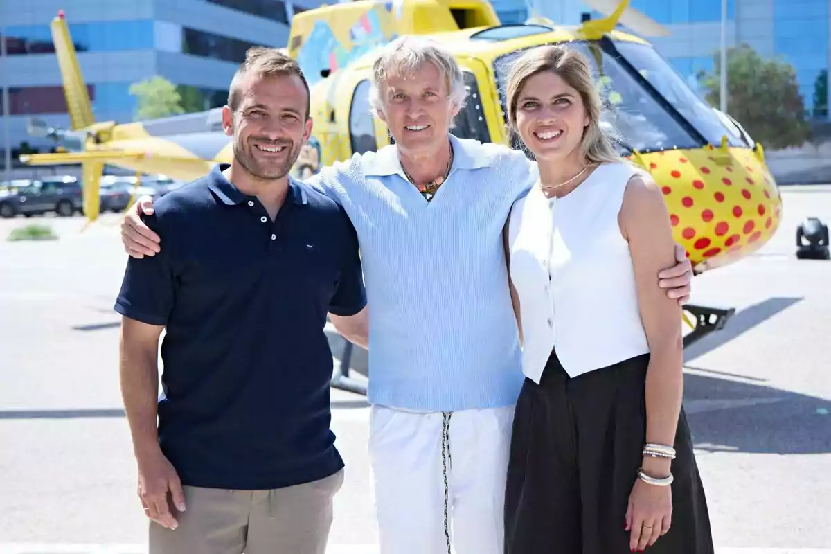 Jesús Calleja, Joan y Sara sonríen abrazadas frente a un helicóptero amarillo decorado con lunares rojos en un entorno urbano y soleado ante el estreno de Volando voy, volando vengo