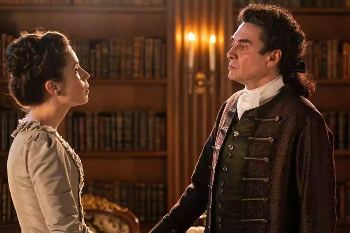 Miren Arrieta y José Manuel Seda vestidos con ropa de época se miran fijamente en una biblioteca elegante iluminada por candelabros en Valle Salvaje. Miren Arrieta y José Manuel Seda vestidos con ropa de época se miran fijamente en una biblioteca elegante iluminada por candelabros en Valle Salvaje.