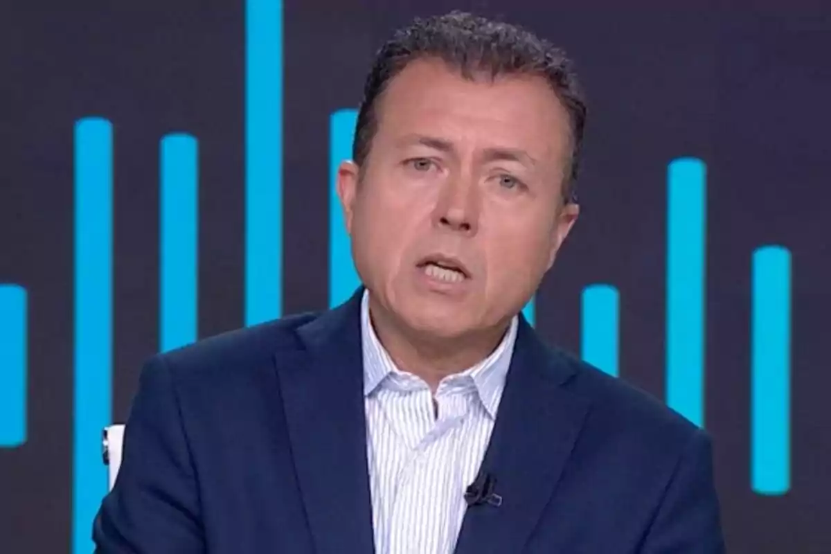 Manu Sánchez Fernández de cabello corto y oscuro con saco azul y camisa clara hablando frente a un fondo con barras verticales azules en Antena 3 Noticias.