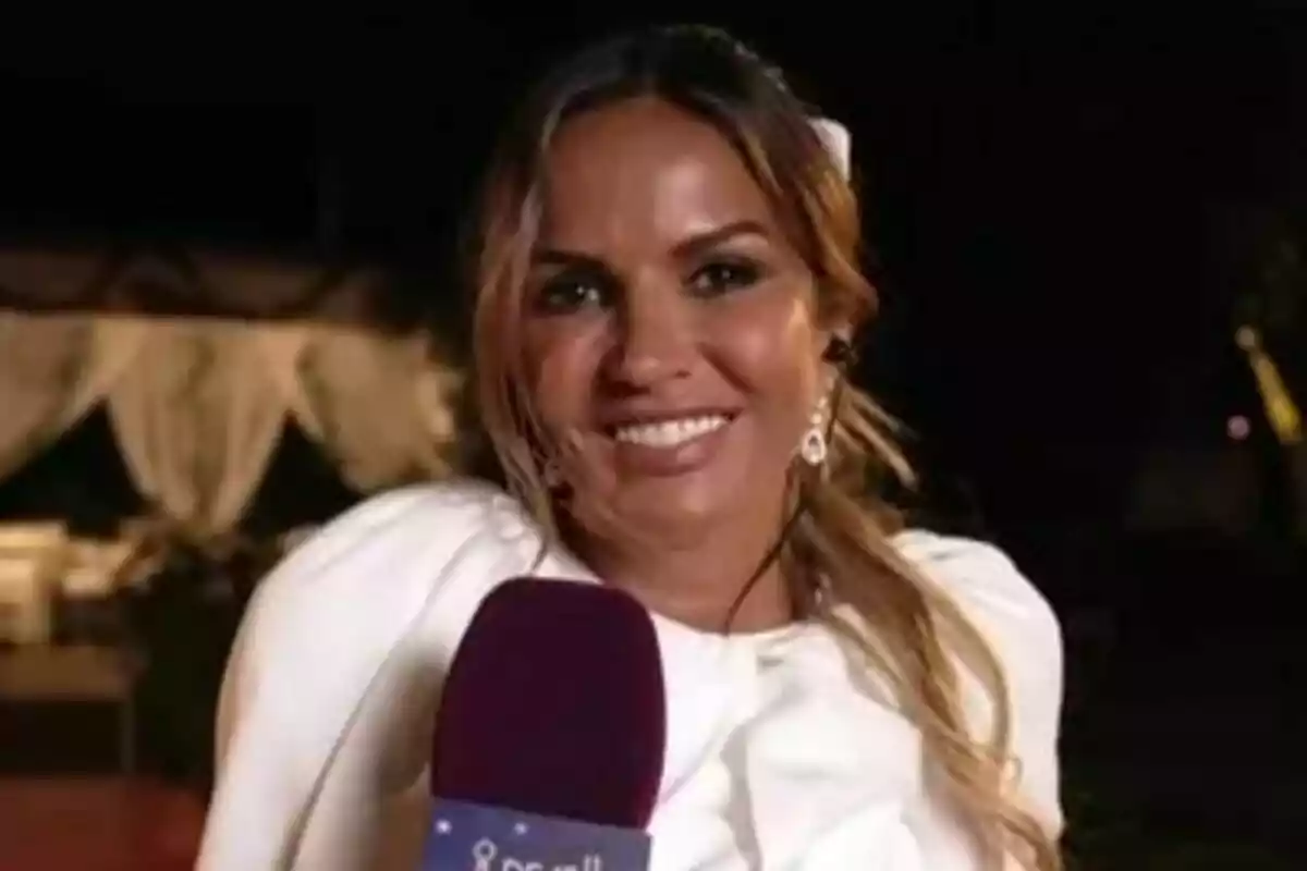 Marta López sonriente con micrófono de De Viernes en la mano vestida de blanco en un evento nocturno al aire libre