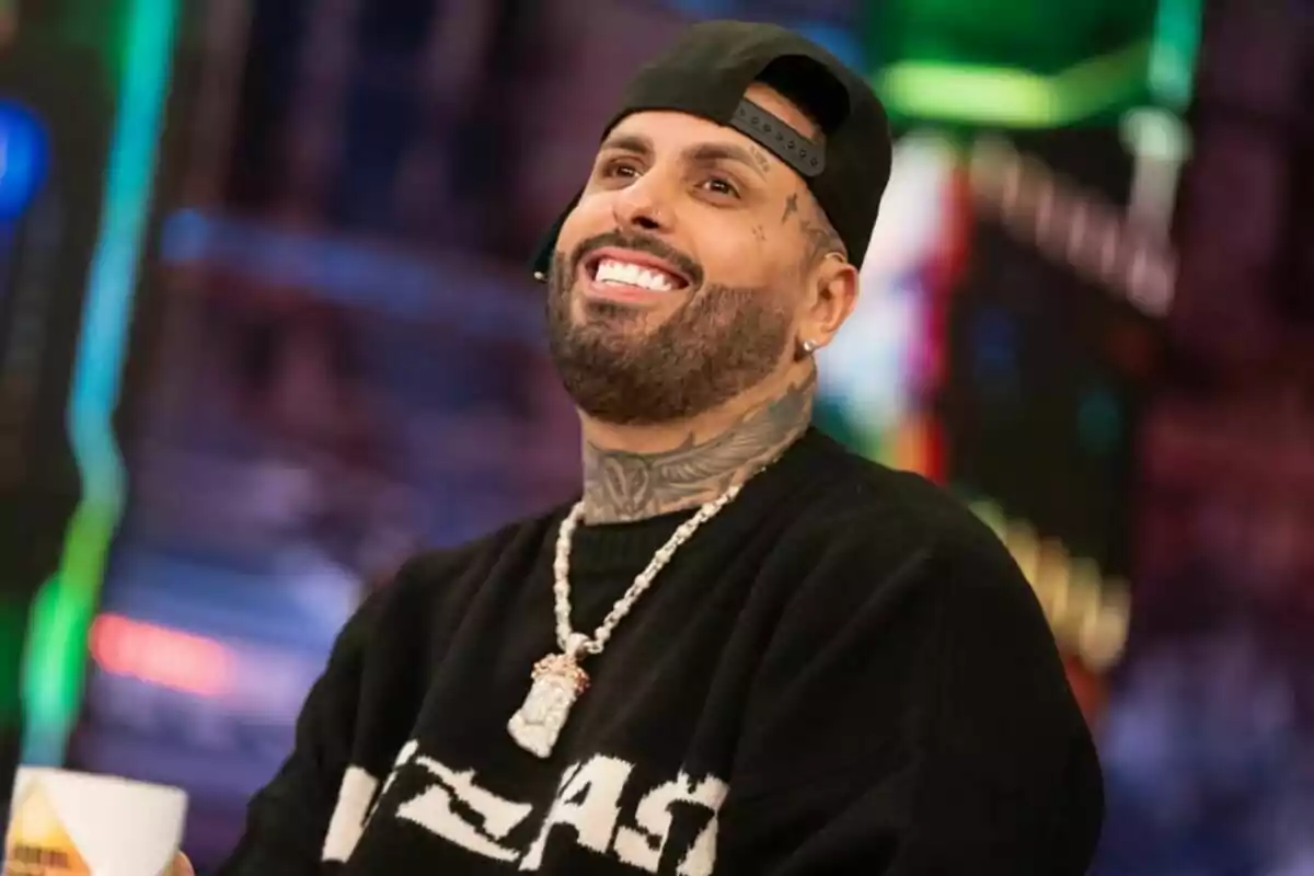 Nicky Jam con barba y gorra negra al revés sonriendo en un ambiente colorido y moderno en 'El Hormiguero'