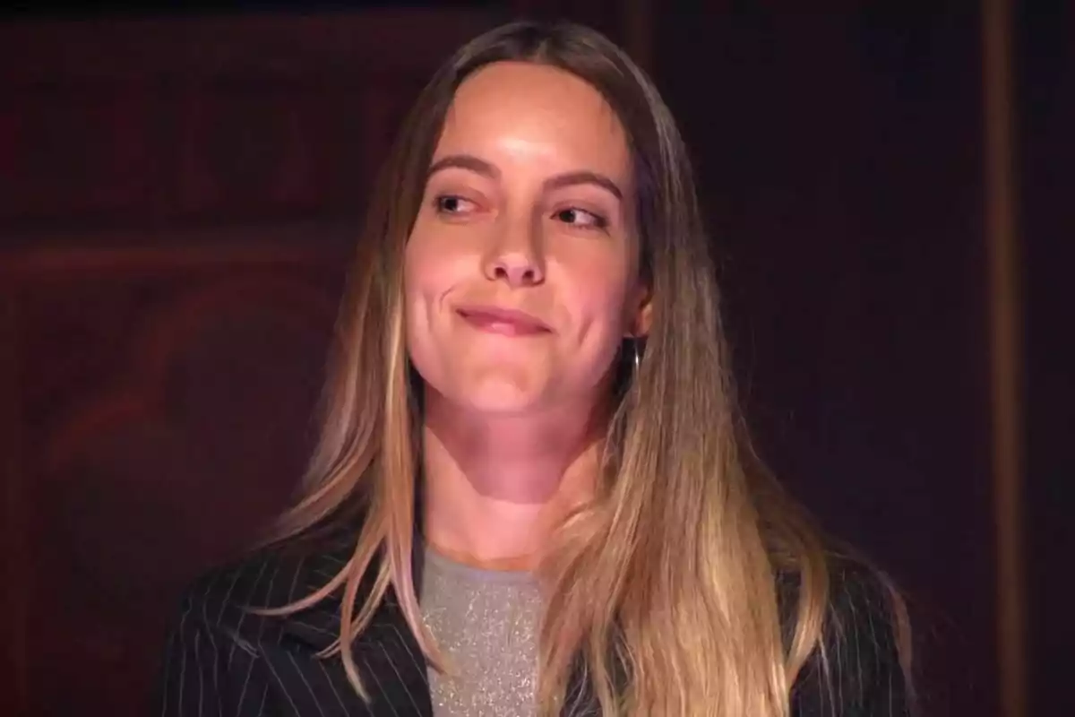 Paula, jove de cabell llarg i ros, amb expressió pensativa i un lleu somriure, mirant cap a un costat en un ambient interior amb llum càlida a Traitors. Paula, jove de cabell llarg i ros, amb expressió pensativa i un lleu somriure, mirant cap a un costat en un ambient interior amb llum càlida a Traitors.