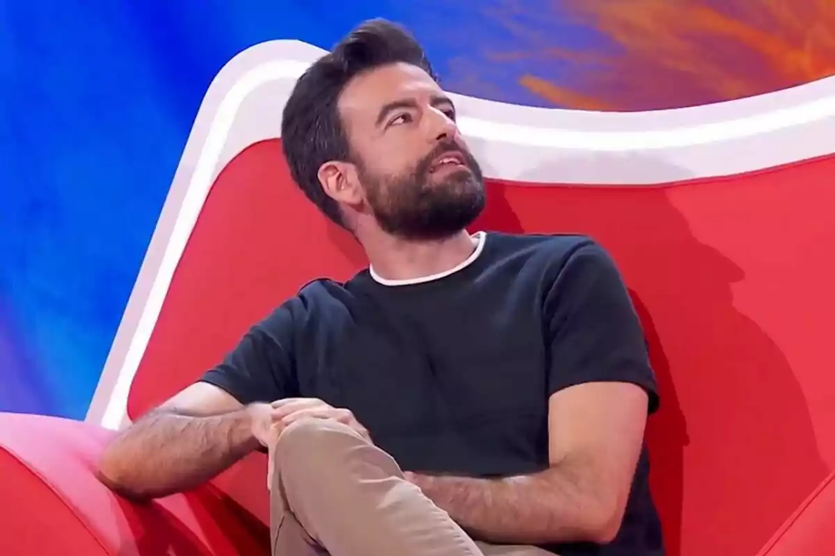 Rafa Castaño con barba sentado en un sillón rojo mirando hacia arriba en un set de Agárrate al sillón colorido Rafa Castaño con barba sentado en un sillón rojo mirando hacia arriba en un set de Agárrate al sillón colorido