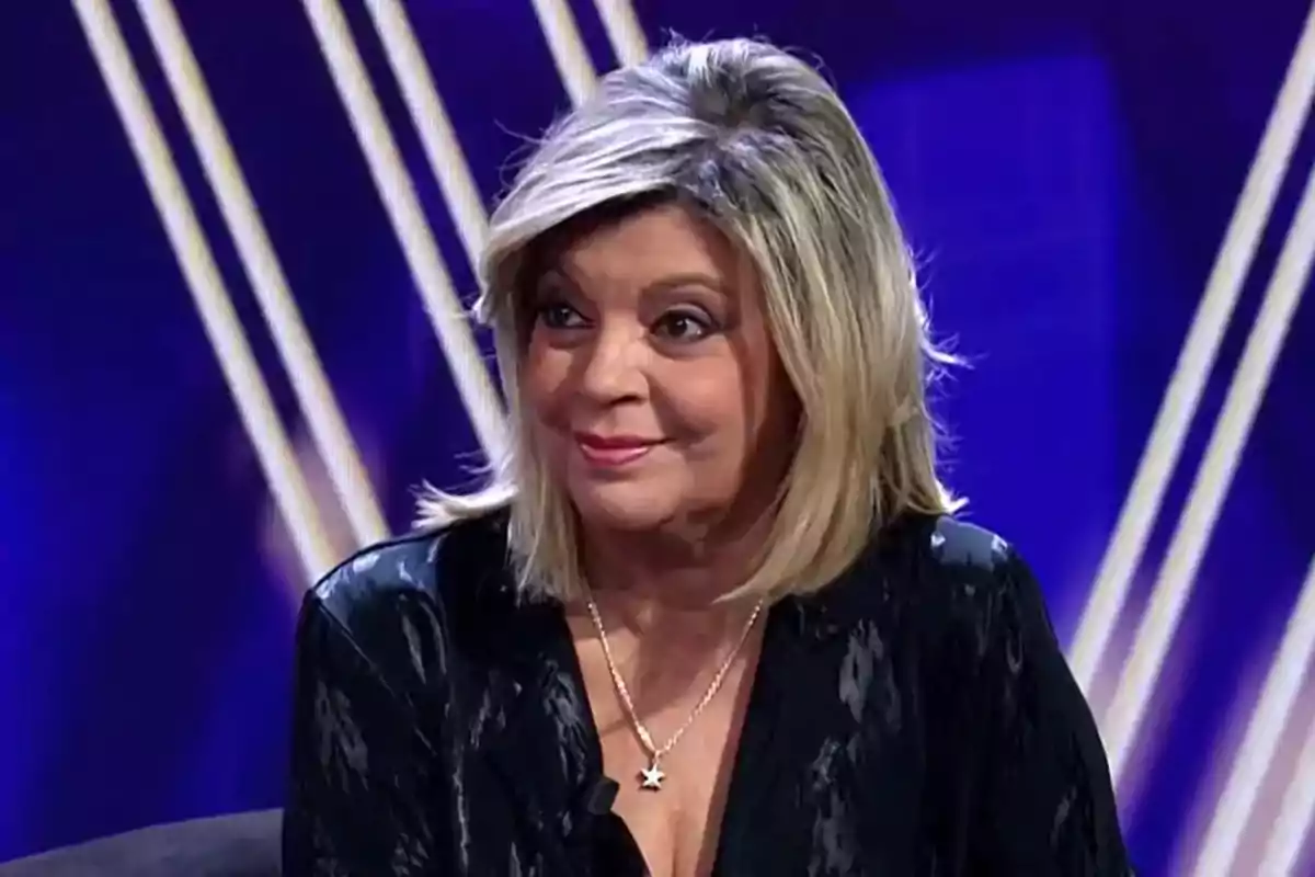 Terelu Campos de cabell ros i curt amb un collaret d’estrella asseguda en un plató de televisió amb fons blau i línies blanques Terelu Campos de cabell ros i curt amb un collaret d’estrella asseguda en un plató de televisió amb fons blau i línies blanques