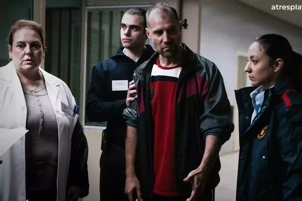 Cuatro personas con expresiones serias están en un pasillo, una de ellas lleva bata blanca, otra uniforme oscuro y José Manuel Poga chaqueta deportiva roja, mientras la cuarta persona parece ser una guardia en 33 días Cuatro personas con expresiones serias están en un pasillo, una de ellas lleva bata blanca, otra uniforme oscuro y José Manuel Poga chaqueta deportiva roja, mientras la cuarta persona parece ser una guardia en 33 días