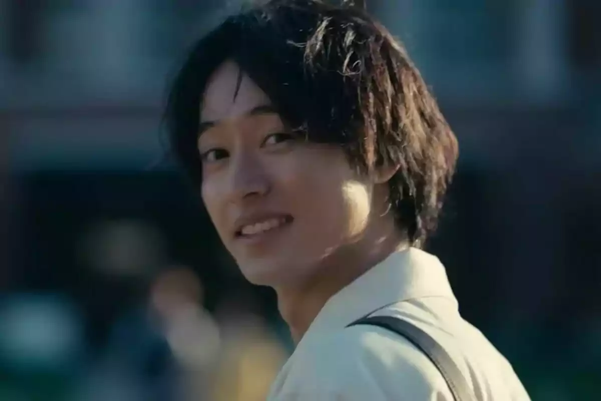 Joven de cabello oscuro mirando hacia atrás y sonriendo en un entorno al aire libre en Alice in Borderland.