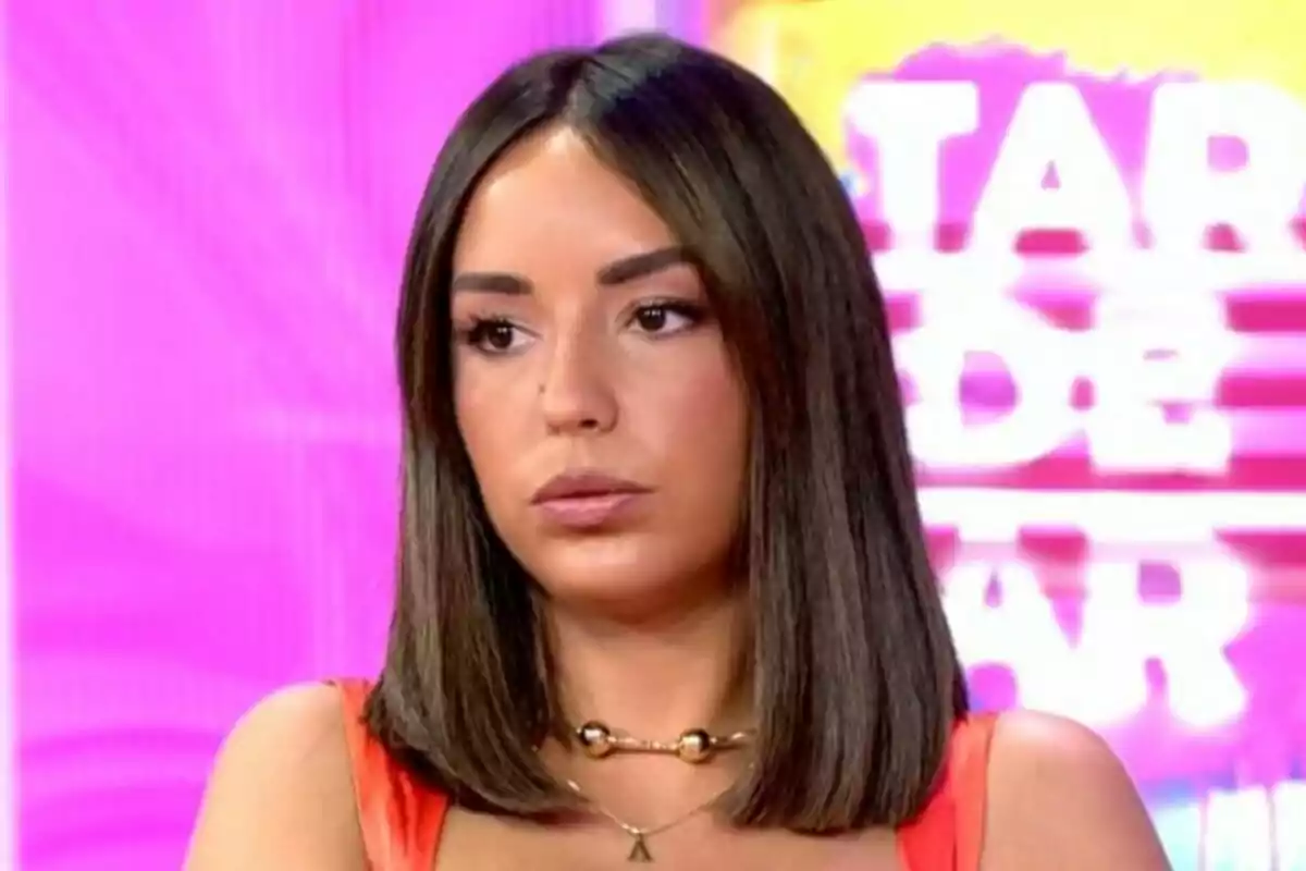 Anita Williams de cabello liso y oscuro con expresión seria sentada frente a un fondo colorido con letras desenfocadas en Tardear. Anita Williams de cabello liso y oscuro con expresión seria sentada frente a un fondo colorido con letras desenfocadas en Tardear.