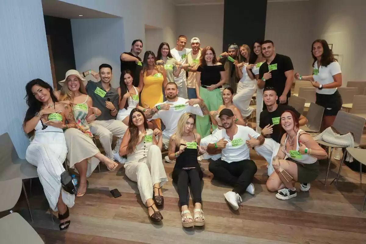 Grupo de personas jóvenes posando sonrientes en una sala, la mayoría sentados y algunos de pie, todos mostrando carteles verdes con números en el casting de Gran Hermano Grupo de personas jóvenes posando sonrientes en una sala, la mayoría sentados y algunos de pie, todos mostrando carteles verdes con números en el casting de Gran Hermano