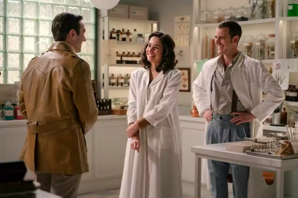 Tres personas conversan y sonríen, que son Beltrán, Cristina y Luis, en el interior de un laboratorio o farmacia antigua, dos de ellas llevan batas blancas y la otra viste una chaqueta marrón en una escena de 'Sueños de Libertad'. Tres personas conversan y sonríen, que son Beltrán, Cristina y Luis, en el interior de un laboratorio o farmacia antigua, dos de ellas llevan batas blancas y la otra viste una chaqueta marrón en una escena de 'Sueños de Libertad'.