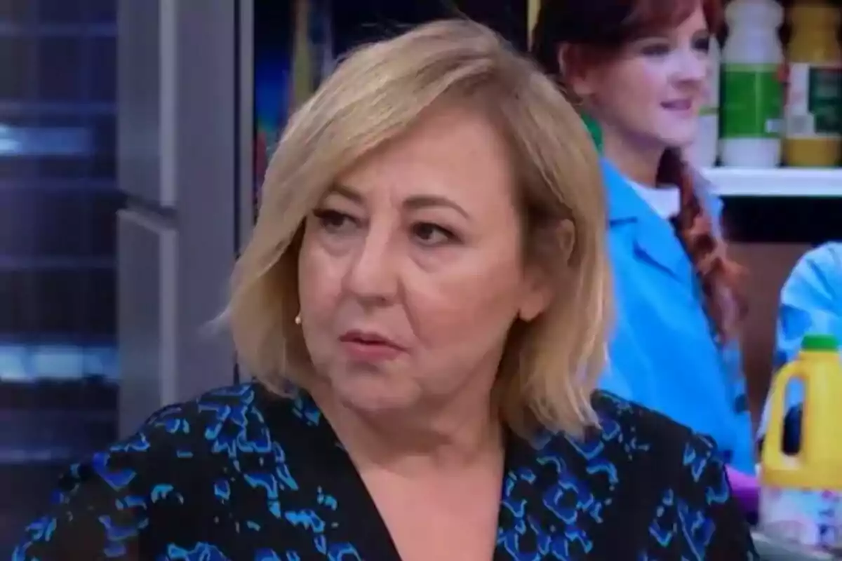 Carmen Machi de cabello rubio corto con expresión seria en un estudio de El Hormiguero con personas y productos de limpieza al fondo