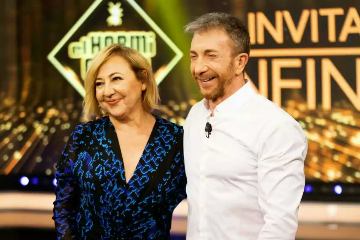 Carmen Machi y Pablo Motos sonrientes posan juntas en un set de El Hormiguero con luces y letreros de fondo Carmen Machi y Pablo Motos sonrientes posan juntas en un set de El Hormiguero con luces y letreros de fondo