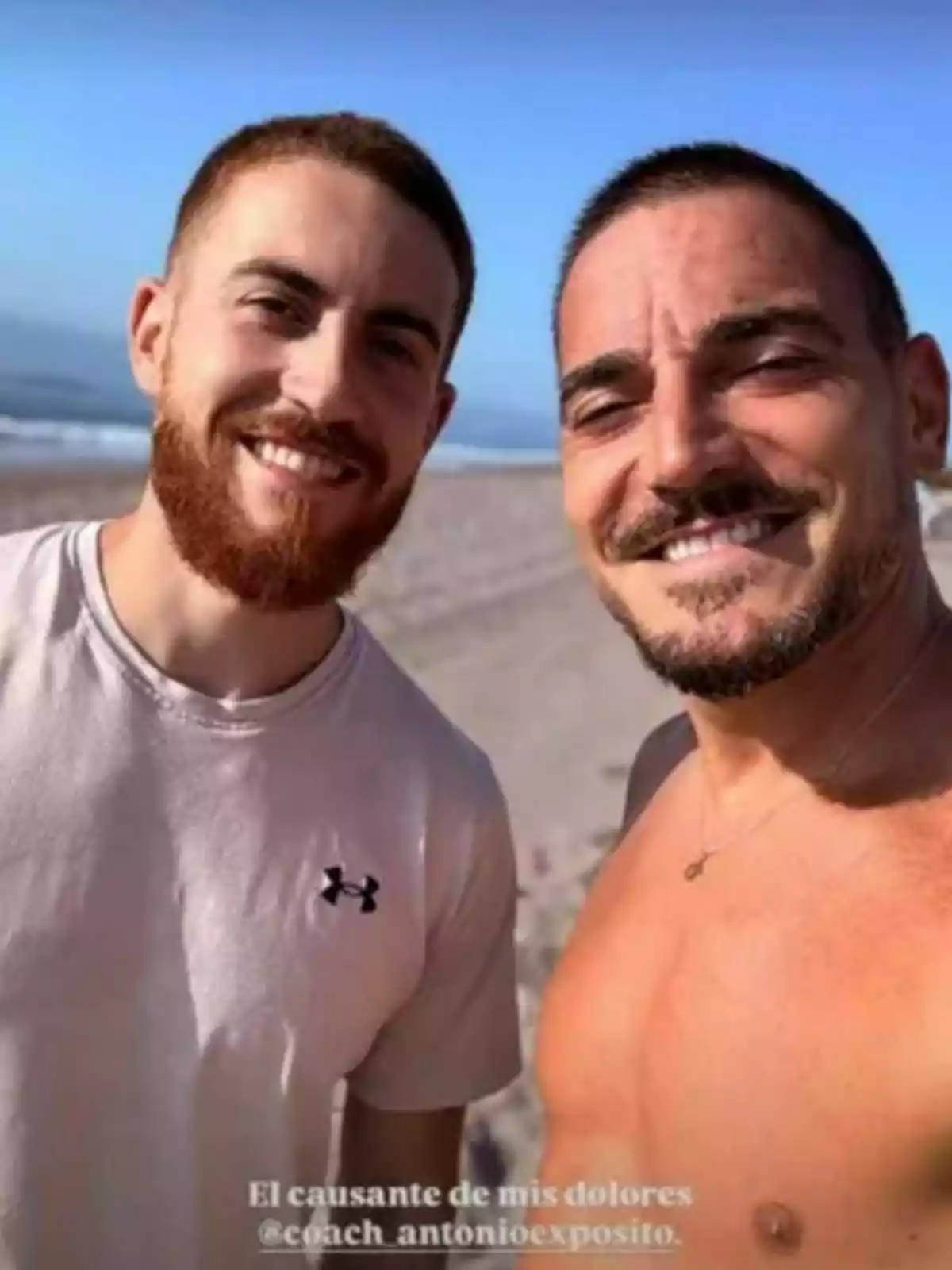 Damián Quintero y otro hombre sonríen mientras se toman una selfie en la playa, uno lleva camiseta clara y el otro está sin camisa, el mar y el cielo azul se ven de fondo. Damián Quintero y otro hombre sonríen mientras se toman una selfie en la playa, uno lleva camiseta clara y el otro está sin camisa, el mar y el cielo azul se ven de fondo.