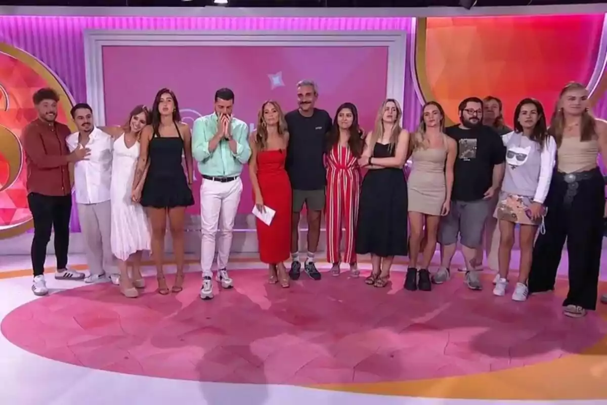 Un grupo de personas en el centro con Antonio Santana y María Verdoy posando juntas en un set de Socialité colorido con fondo rosa y naranja Un grupo de personas en el centro con Antonio Santana y María Verdoy posando juntas en un set de Socialité colorido con fondo rosa y naranja