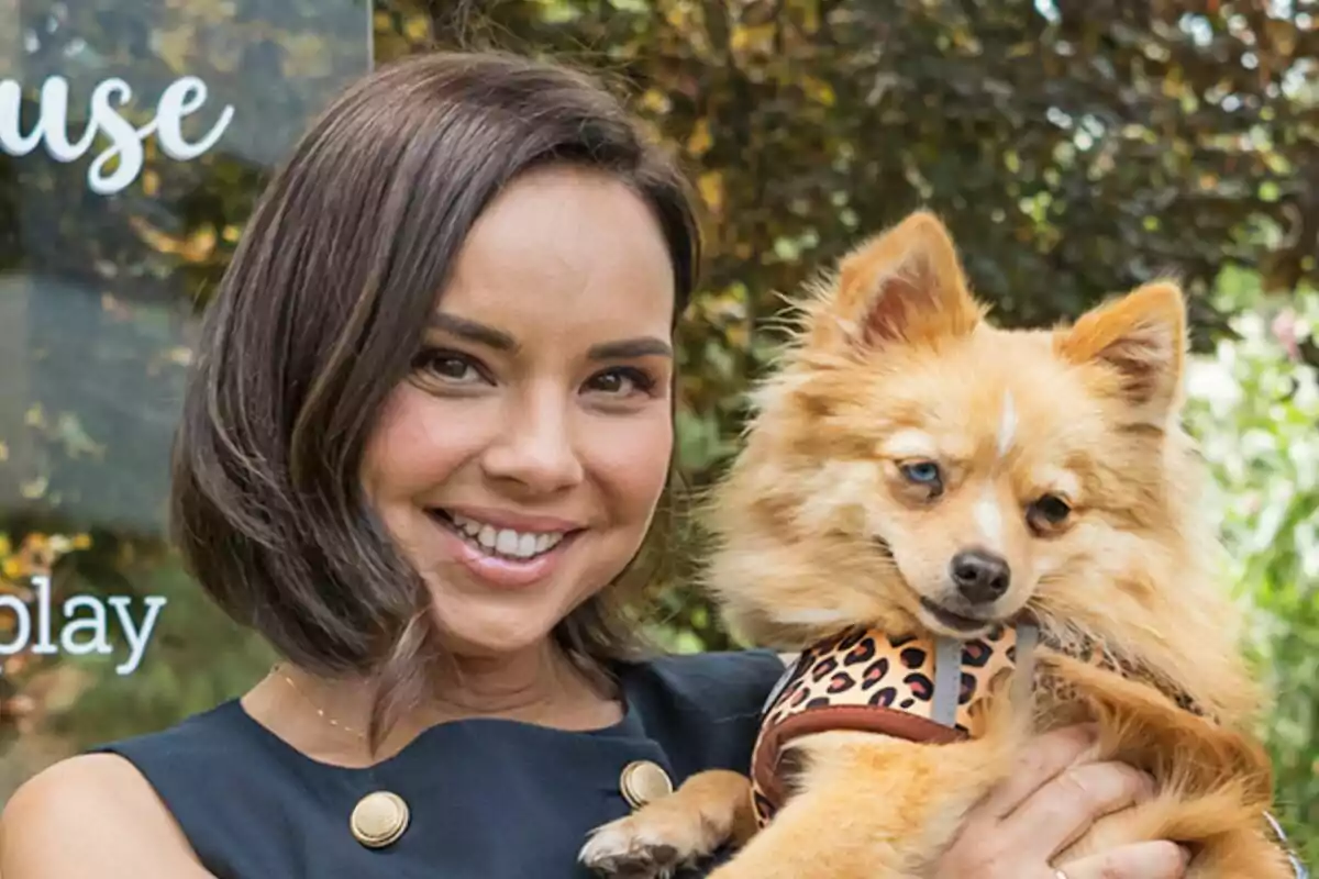 Chenoa sonriente con cabello corto sostiene en brazos a un perro pequeño de pelaje esponjoso y chaleco de estampado animal en la presentación de Dog House