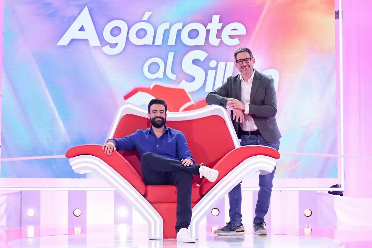 Eugeni Alemany i Rafa Castaño somriuen en un plató de televisió colorit, un assegut en una gran cadira vermella i l’altre dret al seu costat, amb el rètol Agafa’t a la Butaca de fons. Eugeni Alemany i Rafa Castaño somriuen en un plató de televisió colorit, un assegut en una gran cadira vermella i l’altre dret al seu costat, amb el rètol Agafa’t a la Butaca de fons.