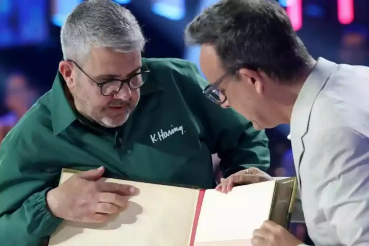 Florentino Fernández i Àngel Llàcer observen atentament un llibre gran de tapa dura en un ambient il·luminat de Tu Cara Me Suena.