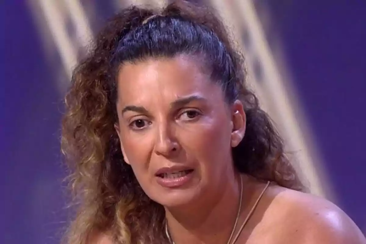 Tamara, hermana de Michu, de cabello rizado recogido con expresión seria en un set de De Viernes con fondo morado.