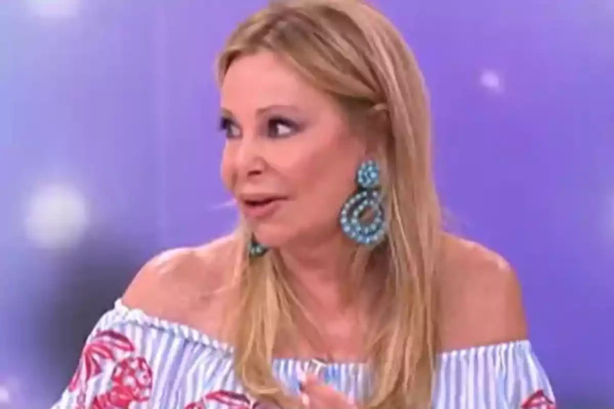 Ana Obregón rubia con el cabello suelto usando unos pendientes grandes de color turquesa y blusa de rayas con hombros descubiertos sobre un fondo morado. Ana Obregón rubia con el cabello suelto usando unos pendientes grandes de color turquesa y blusa de rayas con hombros descubiertos sobre un fondo morado.