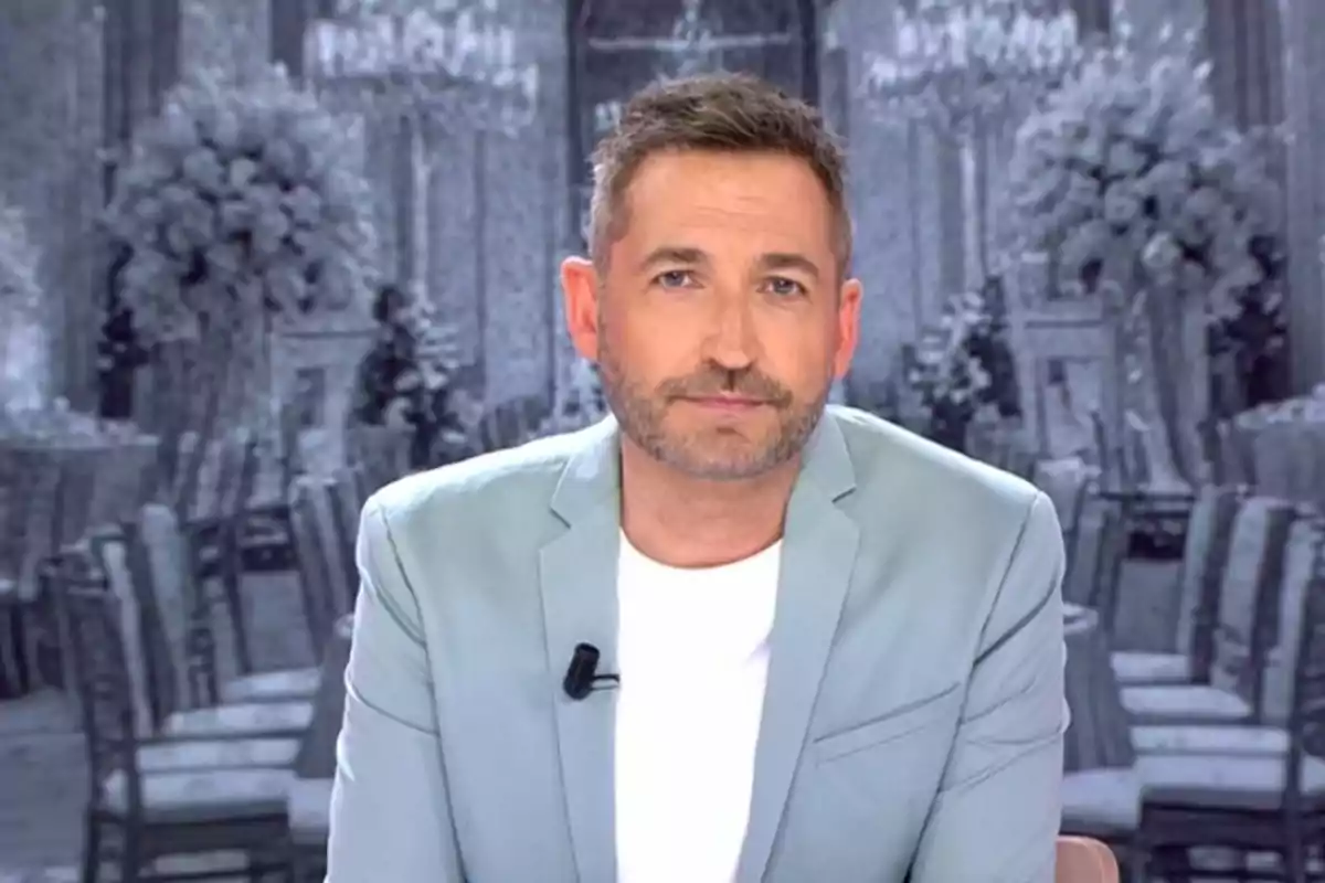 Frank Blanco de cabello corto y barba con chaqueta clara y camiseta blanca sentado frente a un fondo elegante en tonos grises