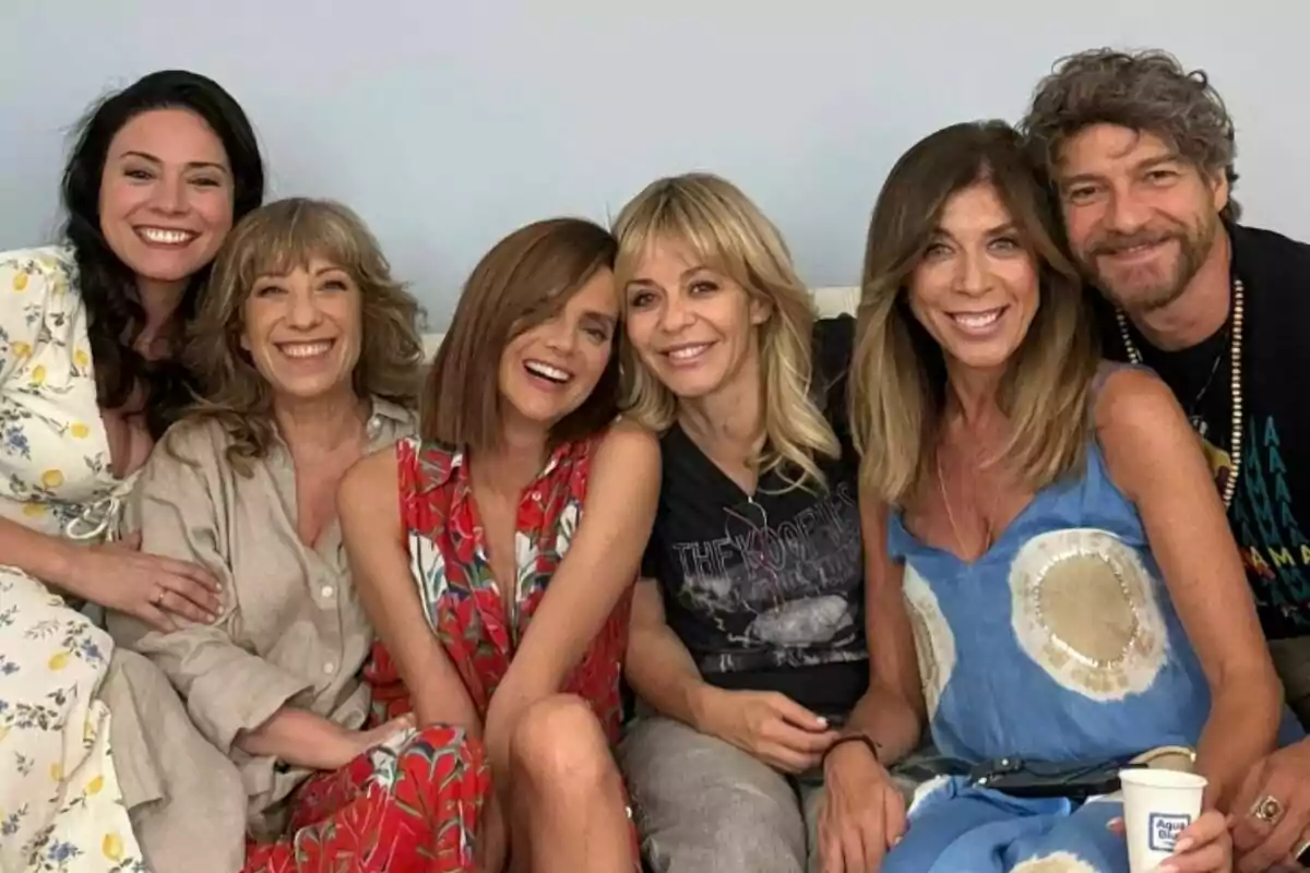 Ana Arias, Nathalie Seseña, Macarena Gómez, María Adánez, Eva Isanta y Félix Gómez sentadas juntas en un sofá sonriendo y abrazándose mientras posan para la foto en el rodaje de La que se avecina