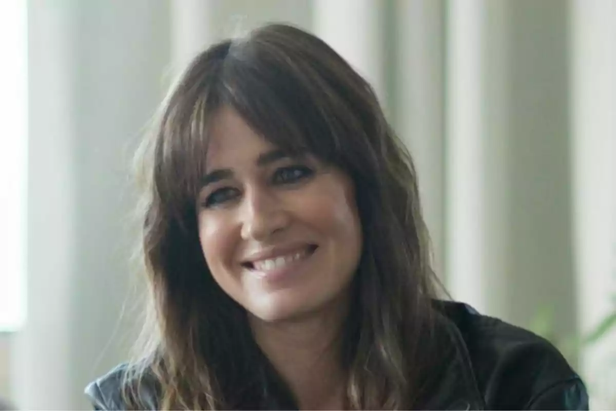 Isabel Jiménez de cabello castaño largo y lacio con flequillo sonriendo y vistiendo una chaqueta oscura en un ambiente interior iluminado en Mis Raíces.