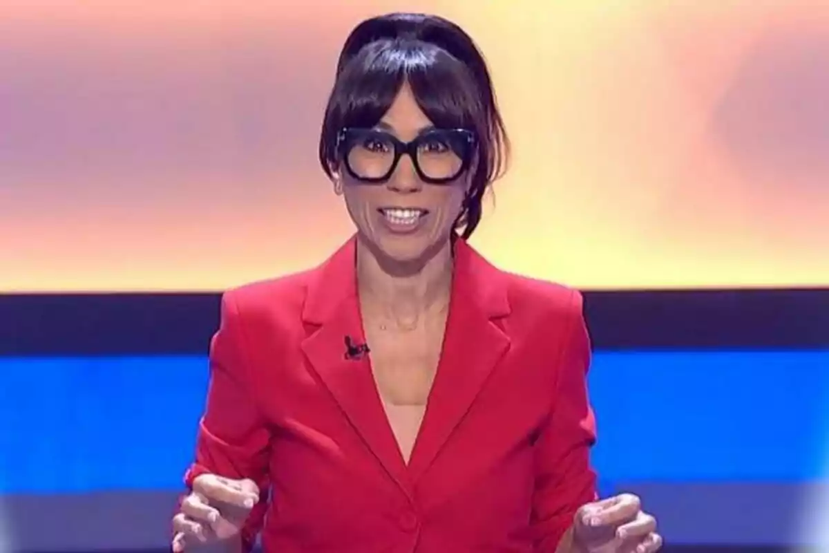 Itziar Miranda amb ulleres grans i cabell fosc recollit porta una jaqueta vermella i està parlant en un plató de La Piràmide amb un fons blau i taronja.