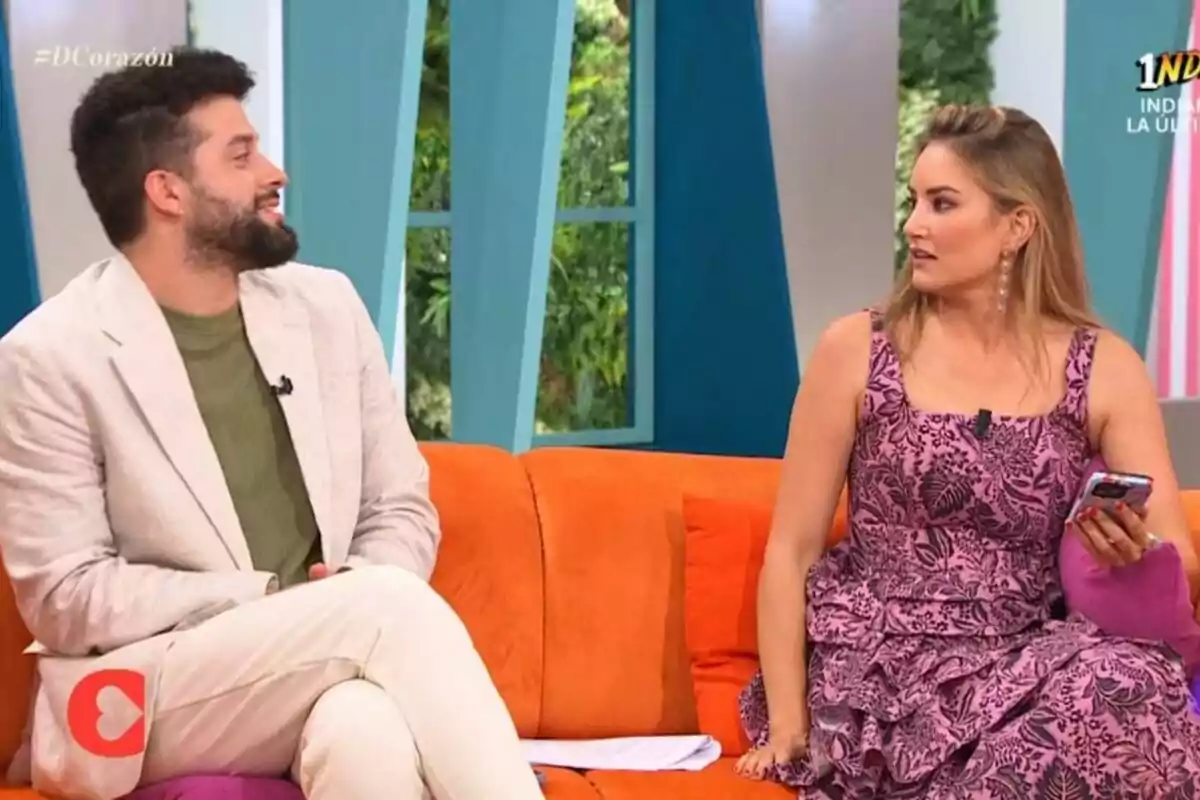 Javi de Hoyos y Alba Carrillo sentados en un sofá naranja durante D Corazón, uno viste traje claro y camiseta verde, la otra lleva un vestido rosa con estampado floral y sostiene un teléfono móvil Javi de Hoyos y Alba Carrillo sentados en un sofá naranja durante D Corazón, uno viste traje claro y camiseta verde, la otra lleva un vestido rosa con estampado floral y sostiene un teléfono móvil