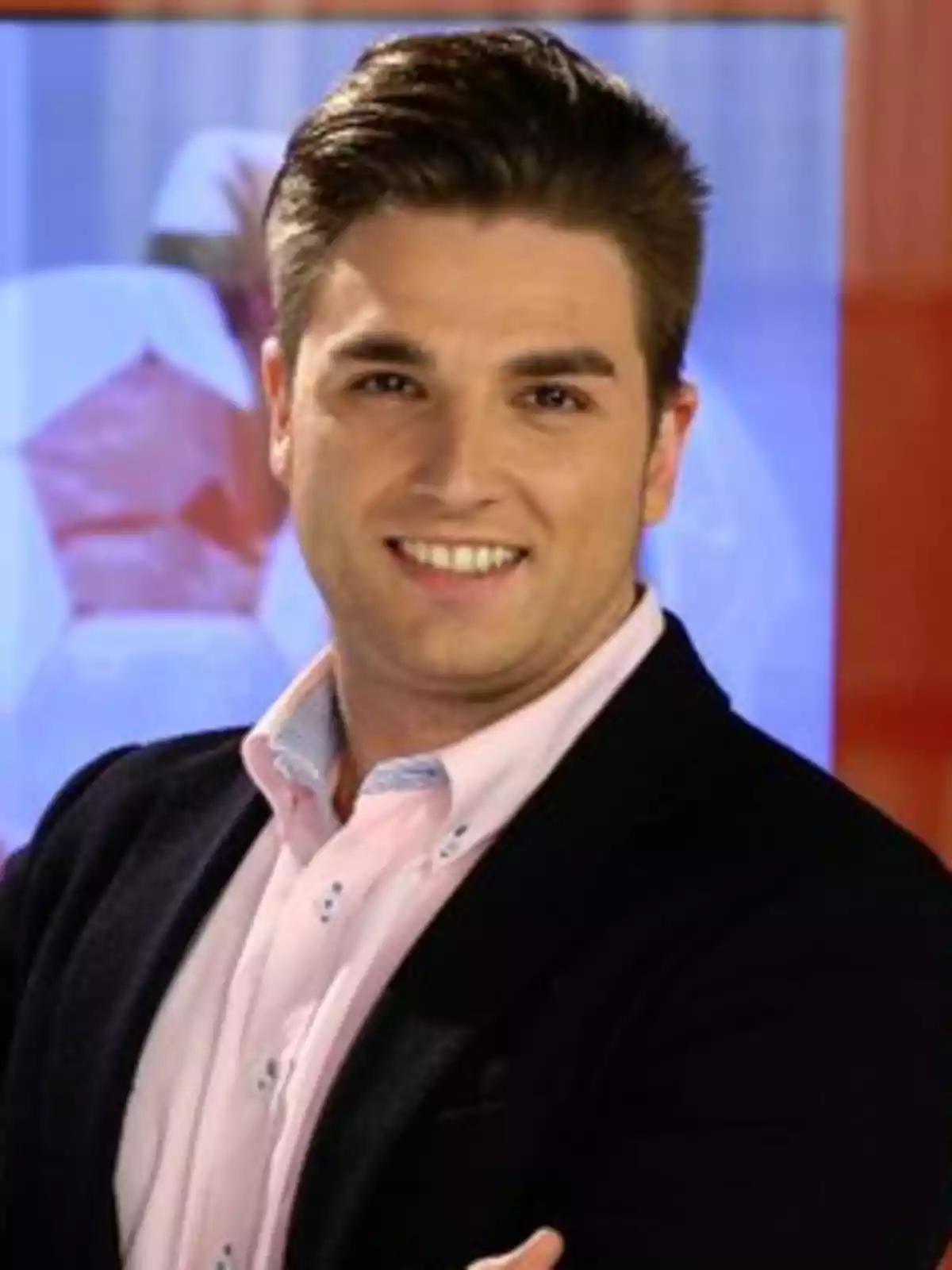Javier Mardones peinado hacia atrás, vistiendo camisa rosa y saco oscuro, sonriendo frente a un fondo desenfocado Javier Mardones peinado hacia atrás, vistiendo camisa rosa y saco oscuro, sonriendo frente a un fondo desenfocado
