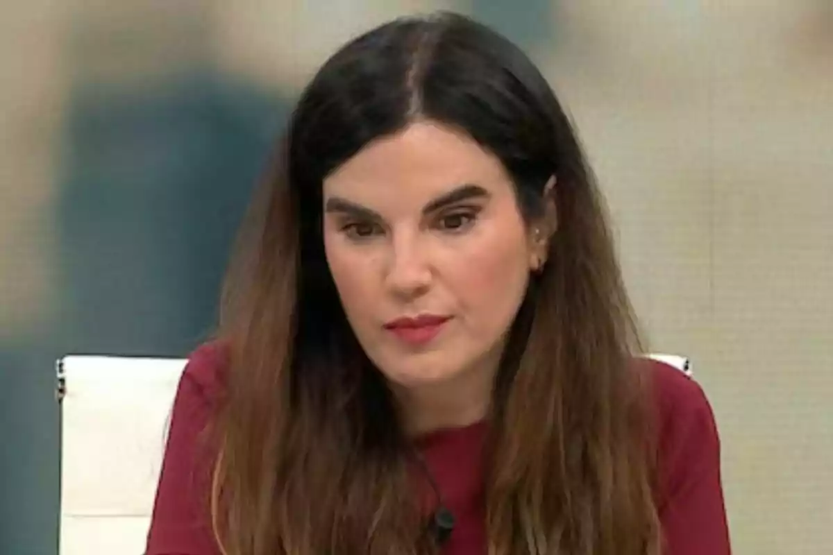 Joanna Ivars de cabell llarg i fosc amb expressió seriosa asseguda en una cadira blanca a Más Vale Tarde i vestint una brusa de color vi