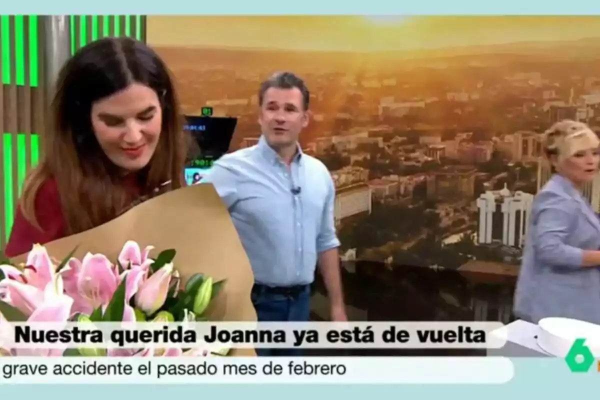 Joanna Ivars sosté un ram de flors roses mentre Iñaki López i Cristina Pardo són al fons d’un plató de Más Vale Tarde amb un paisatge urbà i un rètol que dona la benvinguda a la Joanna després d’un accident. Joanna Ivars sosté un ram de flors roses mentre Iñaki López i Cristina Pardo són al fons d’un plató de Más Vale Tarde amb un paisatge urbà i un rètol que dona la benvinguda a la Joanna després d’un accident.