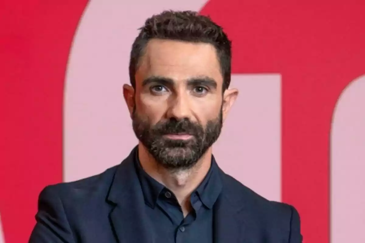Jokin Castellón de cabello corto y barba oscura con saco azul posando frente a un fondo rojo y rosa en laSexta Clave Jokin Castellón de cabello corto y barba oscura con saco azul posando frente a un fondo rojo y rosa en laSexta Clave