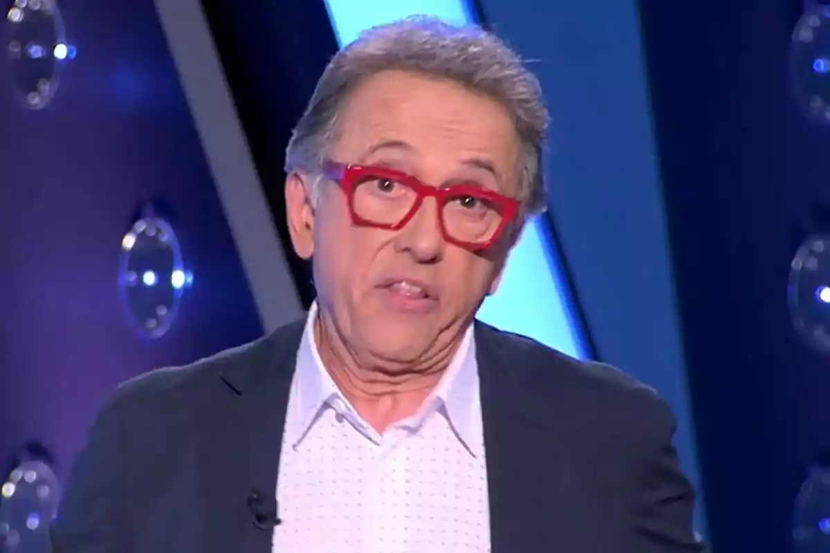 Jordi Hurtado de cabello canoso con gafas rojas y camisa blanca en un set de Saber y Ganar