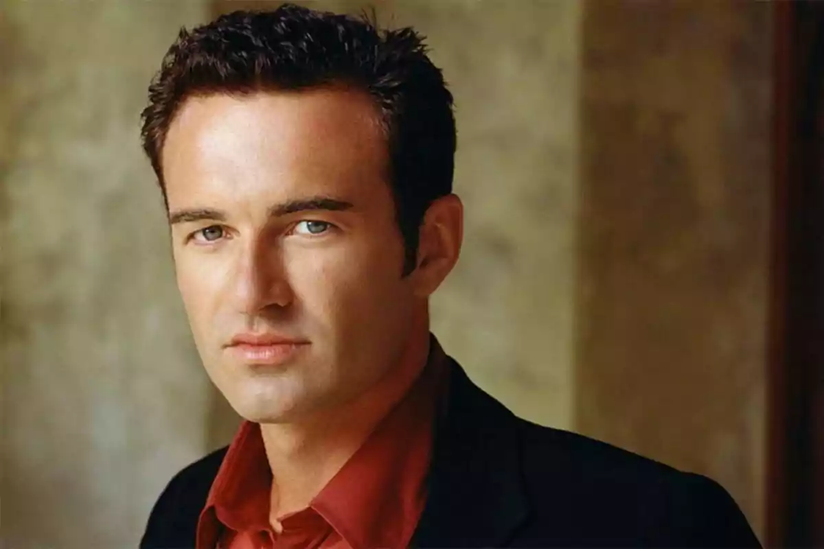 Julian McMahon de cabello oscuro y corto con camisa roja y saco negro mirando a la cámara con expresión seria Julian McMahon de cabello oscuro y corto con camisa roja y saco negro mirando a la cámara con expresión seria
