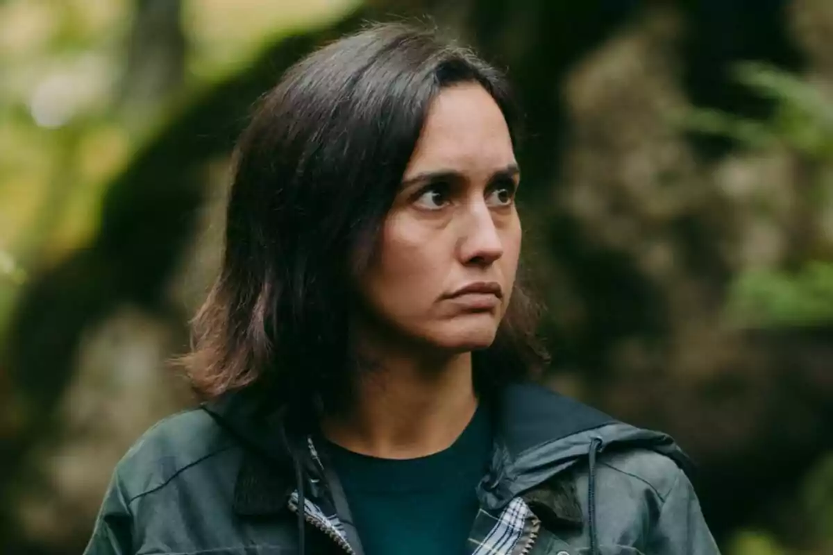 Megan Montaner de cabello oscuro y expresión seria con chaqueta verde en un entorno natural desenfocado en La Caza