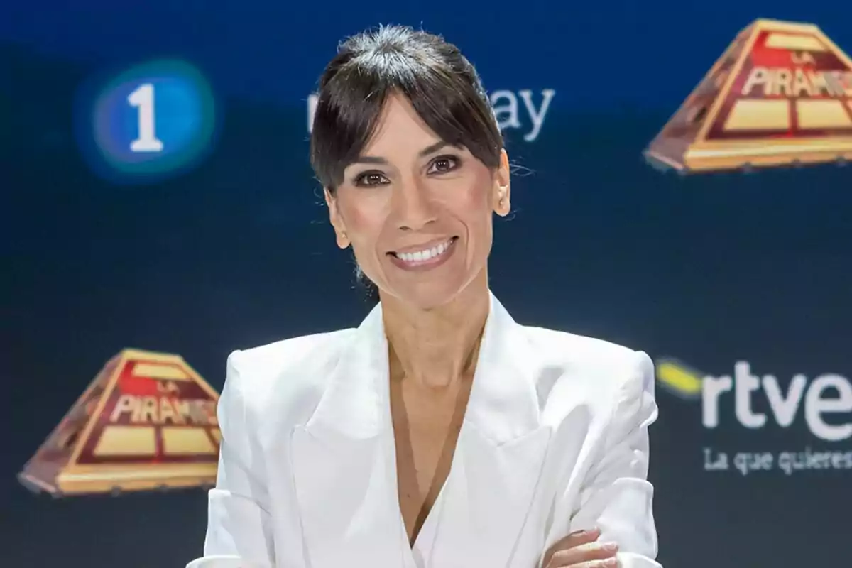 Itziar Miranda de cabell fosc vestida amb jaqueta blanca somrient davant d’un fons blau amb logotips de televisió de La Piràmide