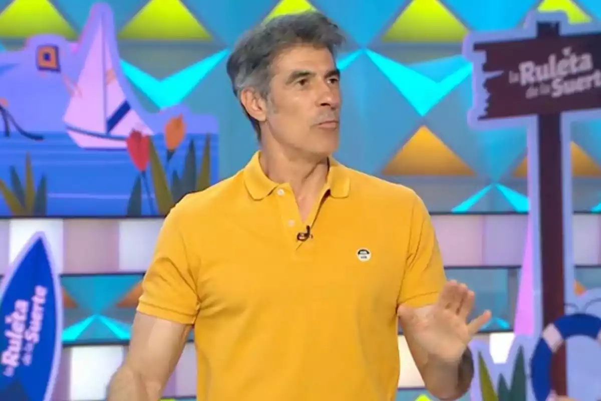 Jorge Fernández con camiseta amarilla en un set colorido de televisión con un letrero de La Ruleta de la Suerte al fondo