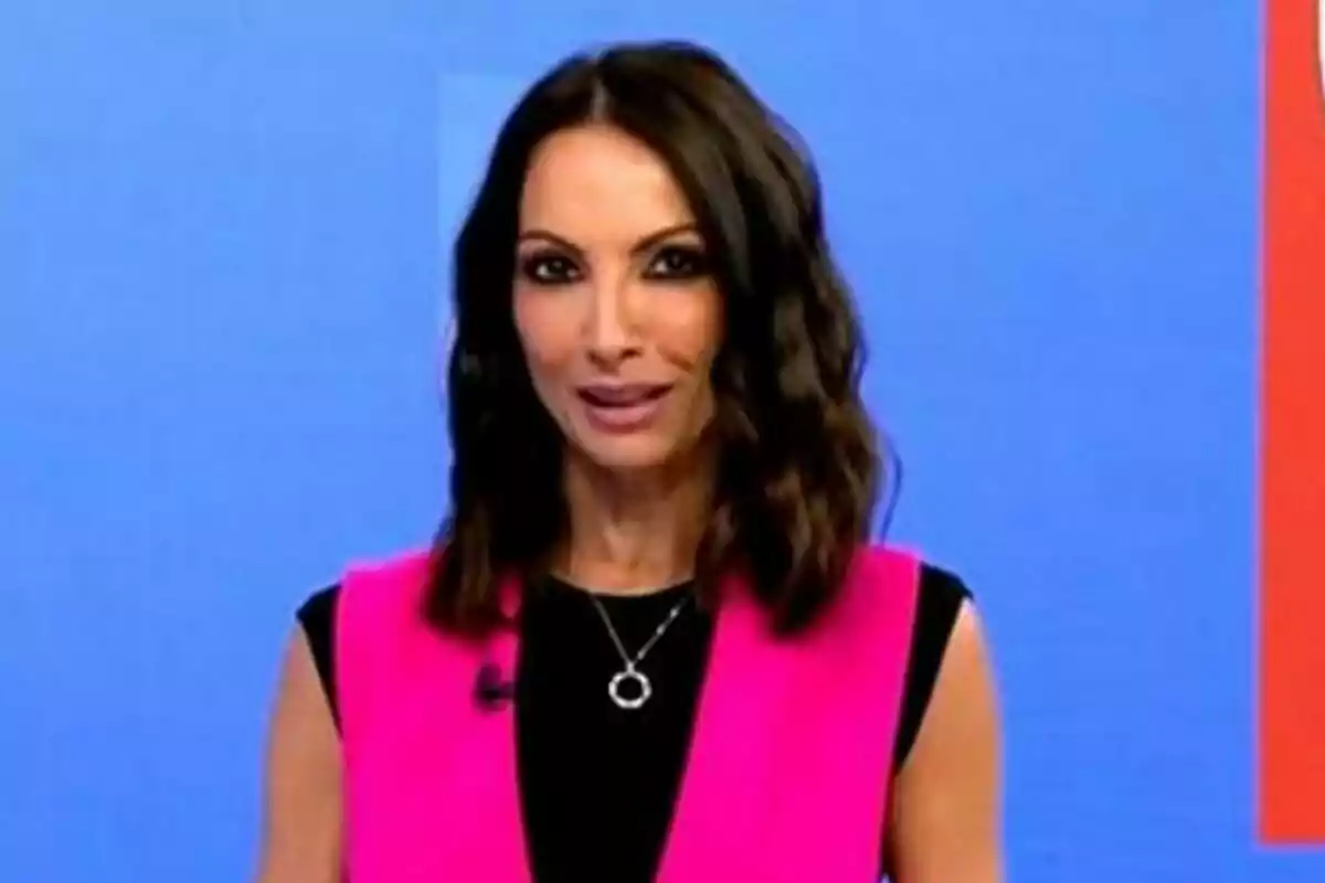Laila Jiménez de cabello oscuro y ondulado usando un chaleco rosa brillante sobre una blusa negra frente a un fondo azul en Informativos Telecinco