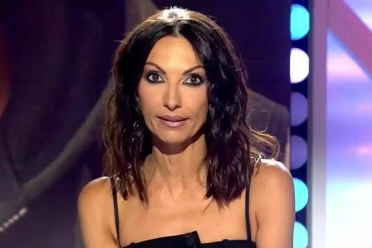 Laila Jiménez de cabello oscuro y ondulado con vestido negro sentada en un set de Todo es Mentira iluminado