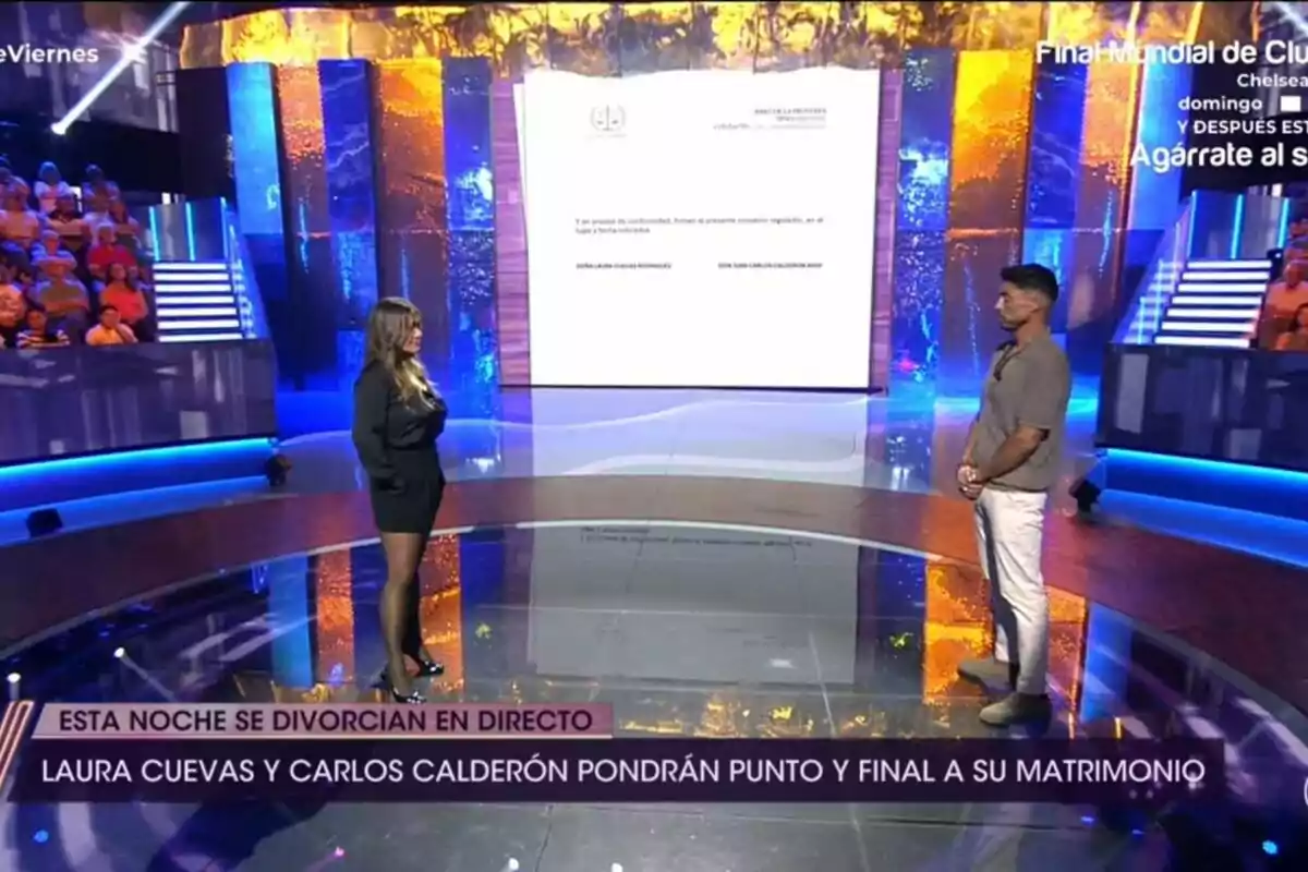 Carlos Calderón i Laura Cuevas estan drets en un escenari de De Divendres amb una gran pantalla al fons i públic assegut als costats, mentre a la part inferior es mostra un anunci sobre un divorci en directe. Carlos Calderón i Laura Cuevas estan drets en un escenari de De Divendres amb una gran pantalla al fons i públic assegut als costats, mentre a la part inferior es mostra un anunci sobre un divorci en directe.