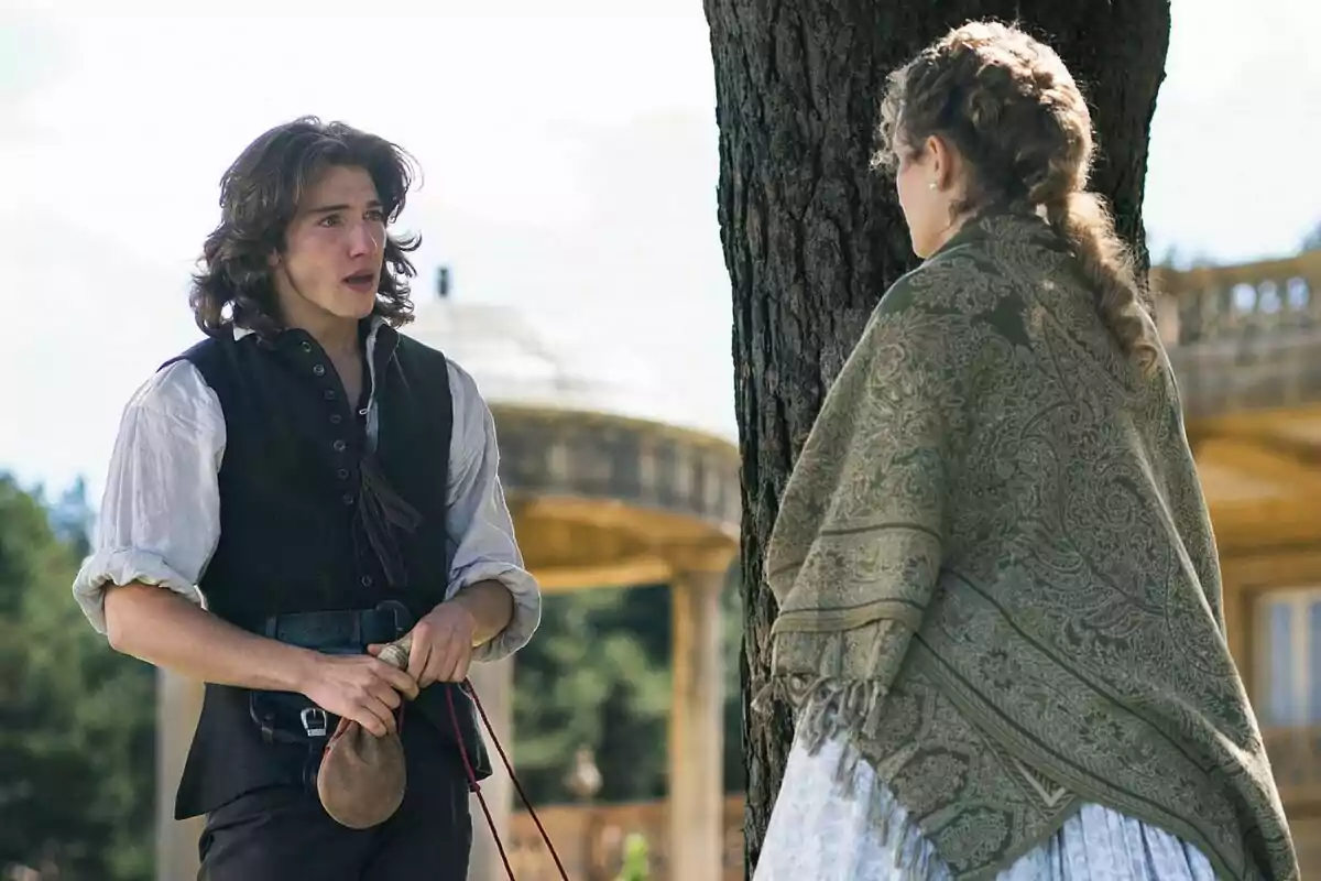 Julen Katzy amb cabell llarg i Emma Guilera amb una trena conversen al costat d’un arbre en un entorn a l’aire lliure amb vestuari d’època a Valle Salvaje. Julen Katzy amb cabell llarg i Emma Guilera amb una trena conversen al costat d’un arbre en un entorn a l’aire lliure amb vestuari d’època a Valle Salvaje.