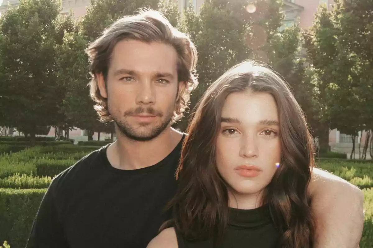Carla Campra y Carlos Cuevas posando juntos al aire libre en un jardín con árboles y arbustos al fondo en Los secretos de la cortesana