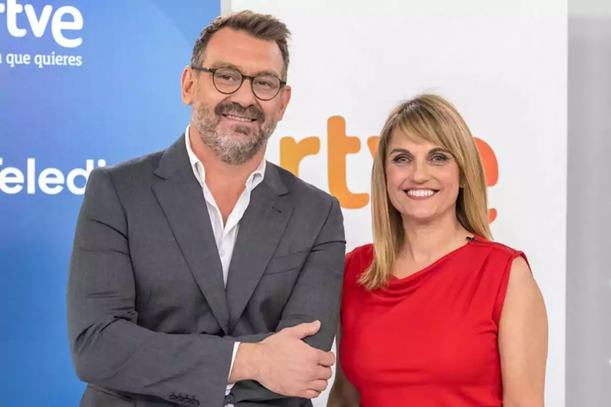 Marc Sala y Lourdes Maldonado sonríen frente a un fondo con logotipos de RTVE uno lleva traje gris y gafas y la otra viste un vestido rojo Marc Sala y Lourdes Maldonado sonríen frente a un fondo con logotipos de RTVE uno lleva traje gris y gafas y la otra viste un vestido rojo