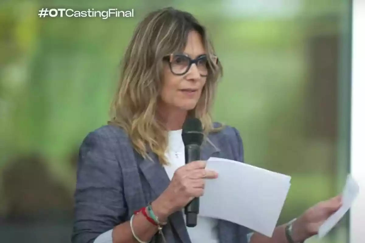 Noemí Galera con gafas y cabello suelto sosteniendo un micrófono y unas hojas mientras habla en un evento con el texto OTCastingFinal en la esquina superior izquierda Noemí Galera con gafas y cabello suelto sosteniendo un micrófono y unas hojas mientras habla en un evento con el texto OTCastingFinal en la esquina superior izquierda