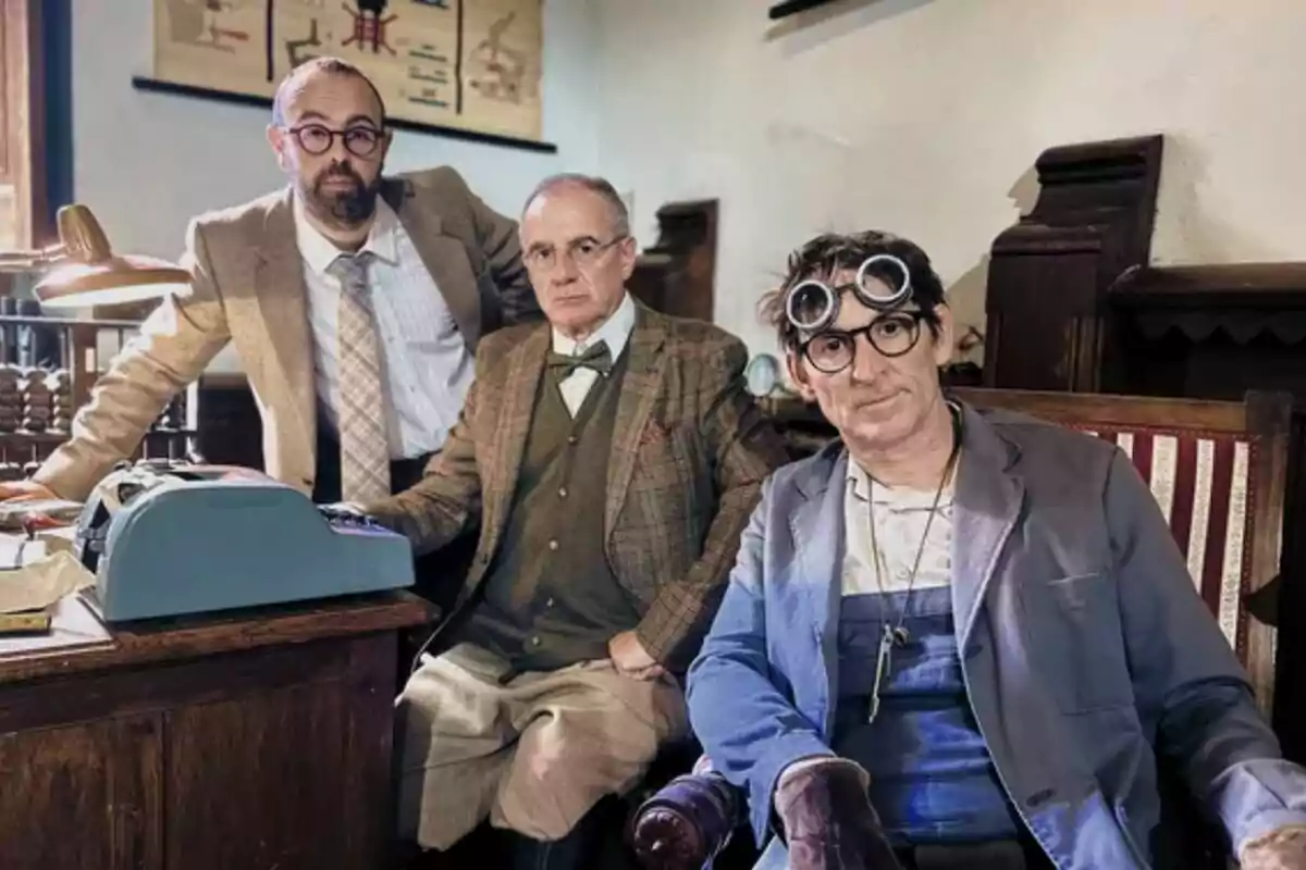 Tres homes vestits amb roba d’època posen en una oficina antiga; un d’ells porta ulleres i guants de treball mentre els altres dos duen vestits formals i una màquina d’escriure és damunt l’escriptori. Tres homes vestits amb roba d’època posen en una oficina antiga; un d’ells porta ulleres i guants de treball mentre els altres dos duen vestits formals i una màquina d’escriure és damunt l’escriptori.