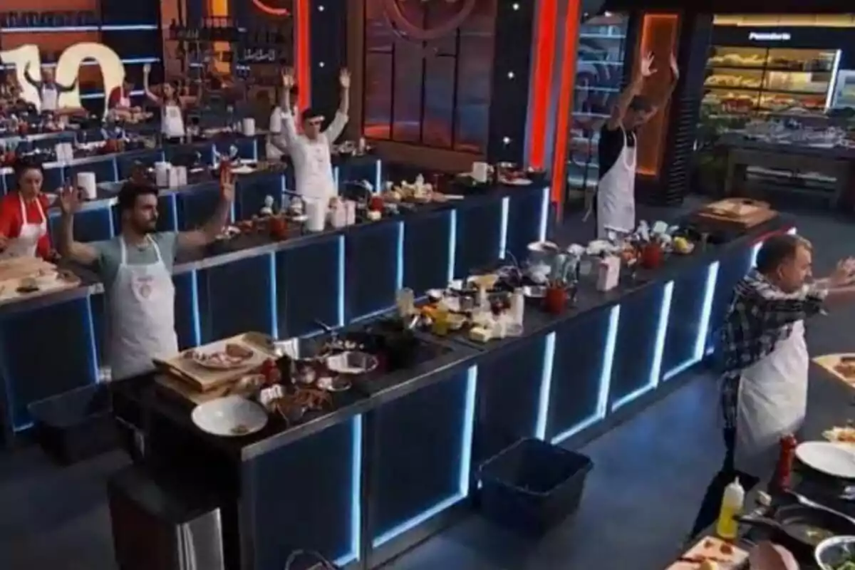 Participantes de un concurso de cocina en MastercChef Celebrity levantan las manos en sus estaciones mientras el tiempo de la competencia termina